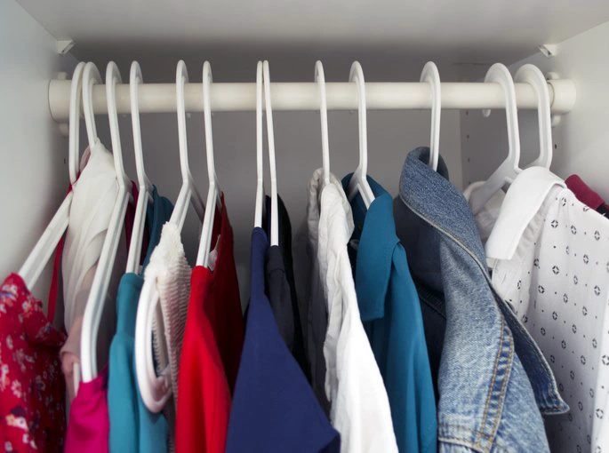 Clothes hanging in a closet, featuring various shirts and a denim jacket on white hangers