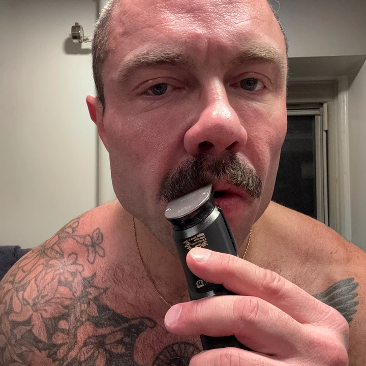 a closeup of a tattooed chest and arm holding a grooming device