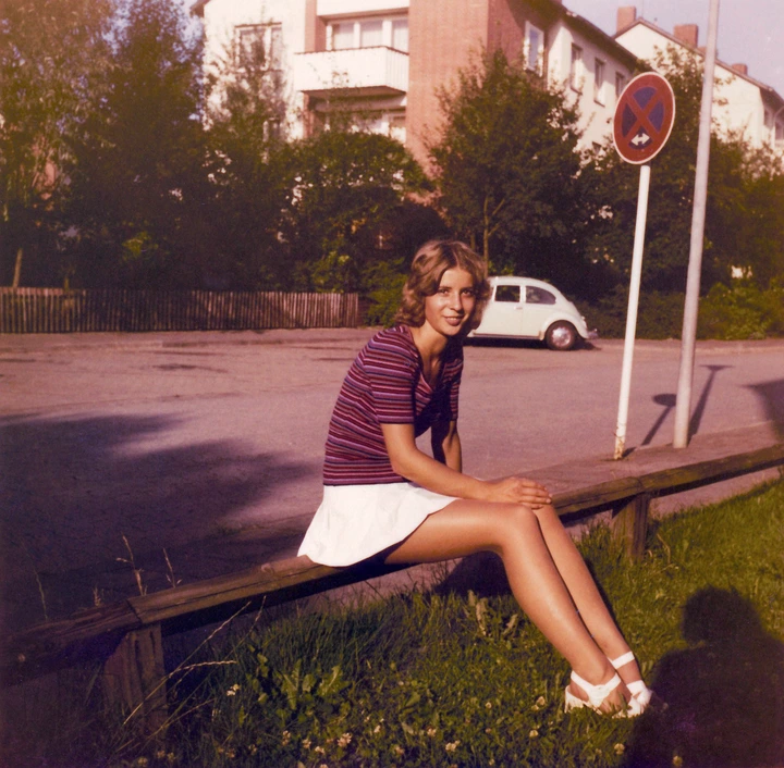 Person sitting on a bench in a residential area, wearing a striped top and white skirt, smiling at the camera