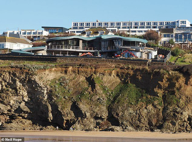 The peculiar house featuring a waterslide roof perches on the edge of the cliff, offering stunning views of the beach below.