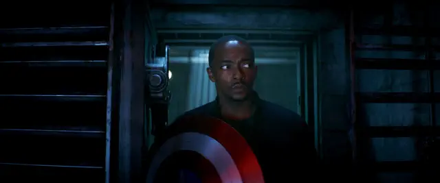 Person holding a round shield, standing in a dimly lit area, looking to the side with a focused expression