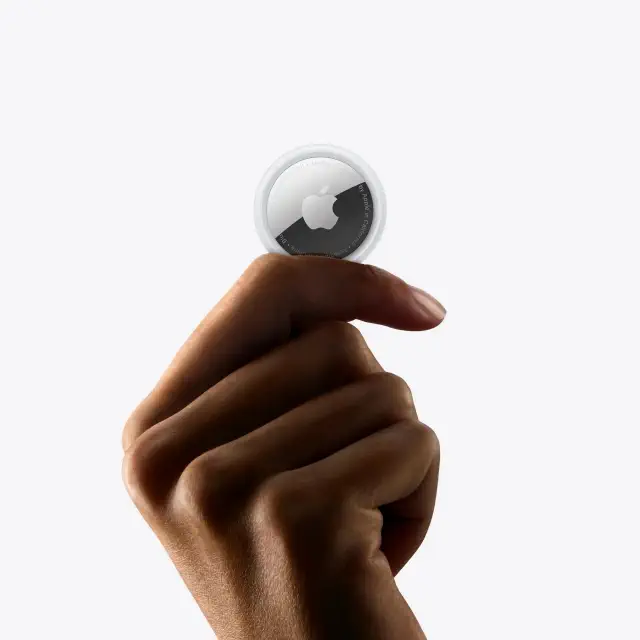 Person holding an Apple AirTag between fingers, showcasing its compact design