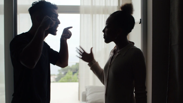 Silhouetted scene of two people in a heated argument, gesturing with hands, in front of a bright window