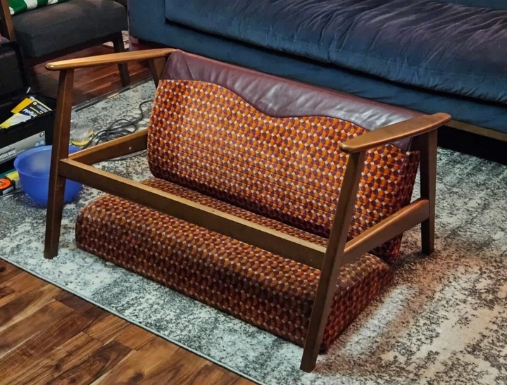 Matthew McCallum A bright orange and red subway seat converted into a couch with wooden armrests and legs in a living room.