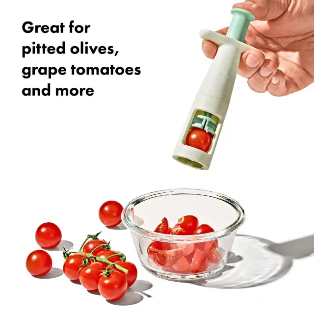 Hand using a kitchen tool to slice cherry tomatoes into a glass bowl; text says, &quot;Great for pitted olives, grape tomatoes, and more.&quot;