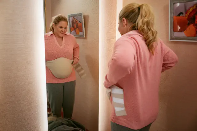 Person wearing a pink sweater and gray pants, adjusting a medical brace in front of a mirror in a cozy room