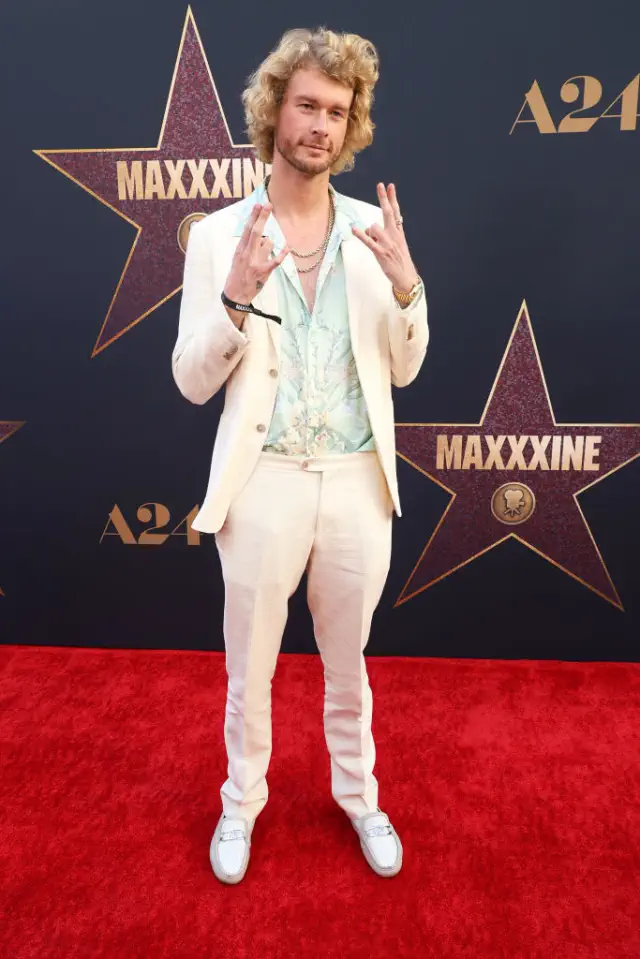 Gravy on red carpet in a suit and floral shirt, making a playful hand gesture, standing in front of star-themed backdrop