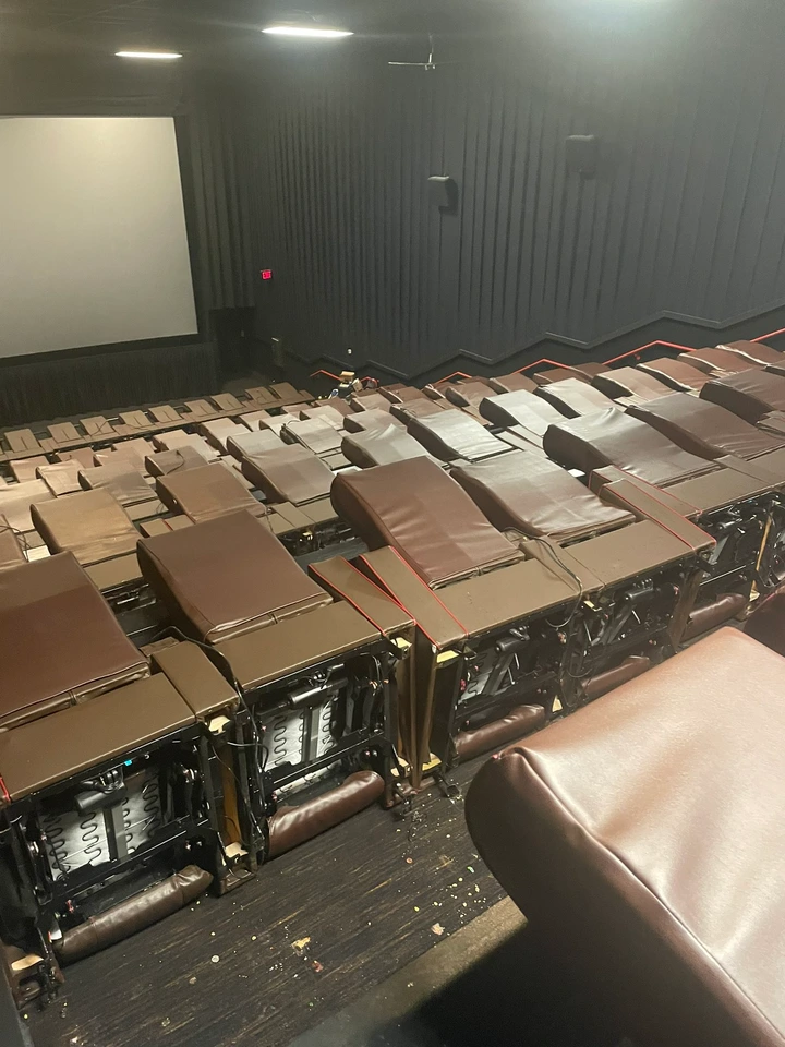 Empty movie theater with rows of recliner seats and a large screen at the front