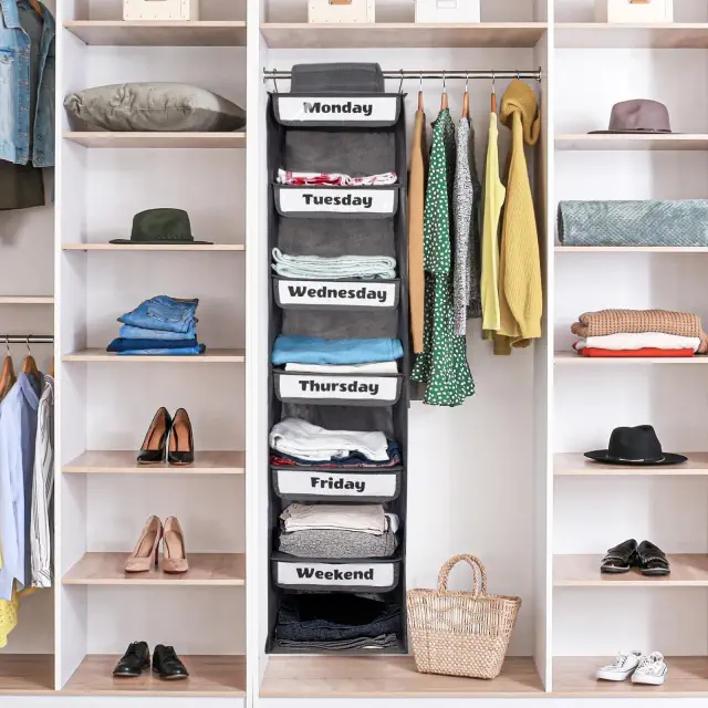 Organized closet with labeled hanging shelves for each day of the week, neatly folded clothes, shoes, hats, and a basket