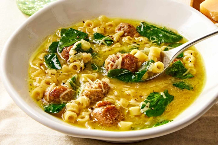 Angled view of a bowl of Italian wedding soup with spoon and topped with Parmesan cheese