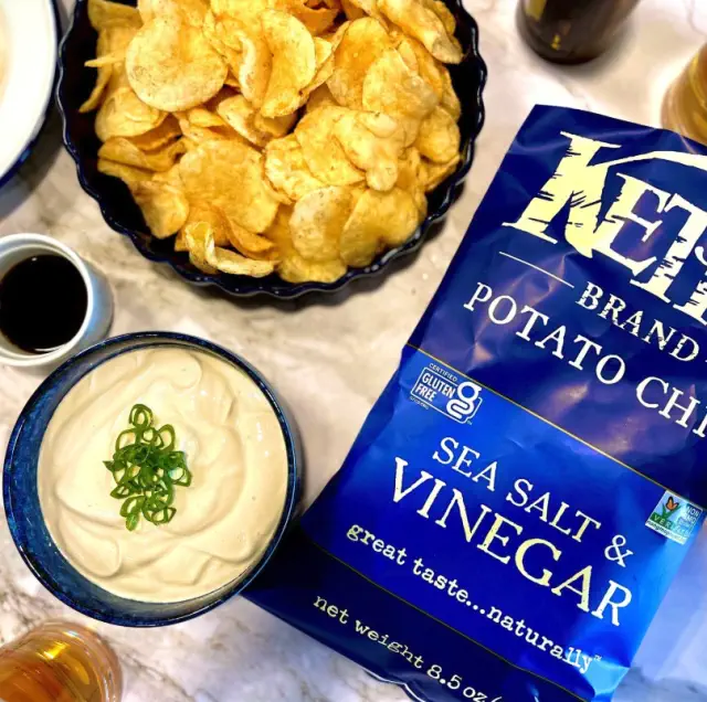 Bag of sea salt and vinegar potato chips on table with dip and snacks