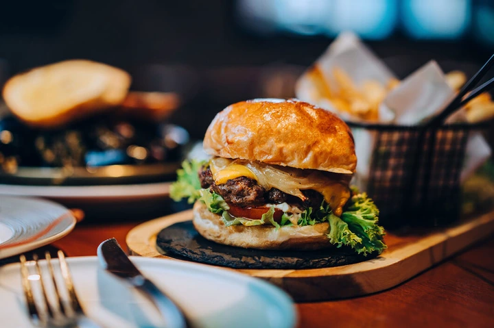 Fresh delicious burger with french fries and salad served on rustic wooden board on table. A feast on the dining table in restaurant. Food and lifestyle concept