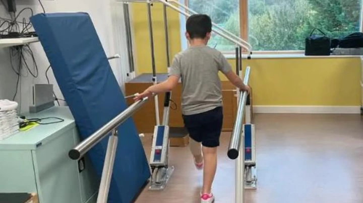 Family pamphlet/PA Real Life Harry is seen walking on a rehabilitation parallel bar setup as part of his physio therapy.