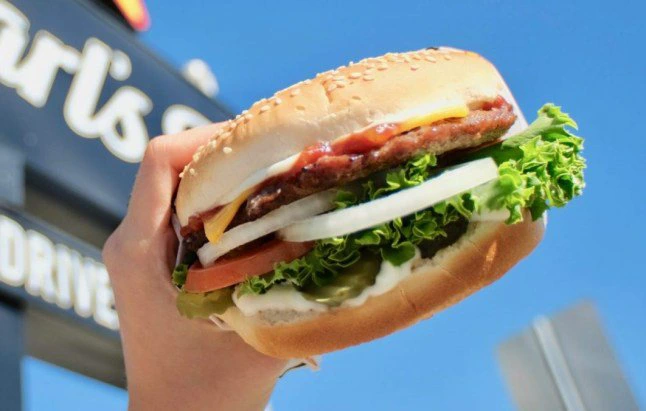 A hand holding a burger in front of a Carl's Jr. sign