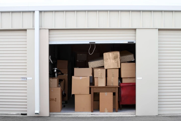 Storage unit filled with cardboard boxes, furniture, and miscellaneous items