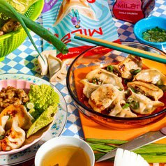 Assorted dumplings on plates with chili crunch, tea, and green onions showcased for a shopping article