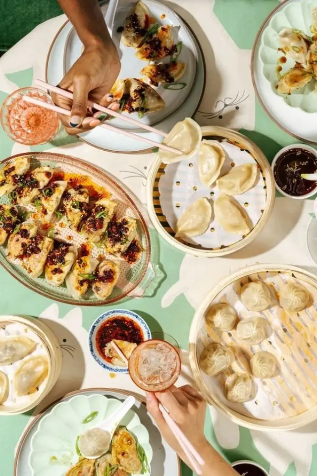 A top-down view of a table filled with various dumplings, dipping sauces, and drinks, with hands reaching in to eat, capturing a vibrant communal dining scene