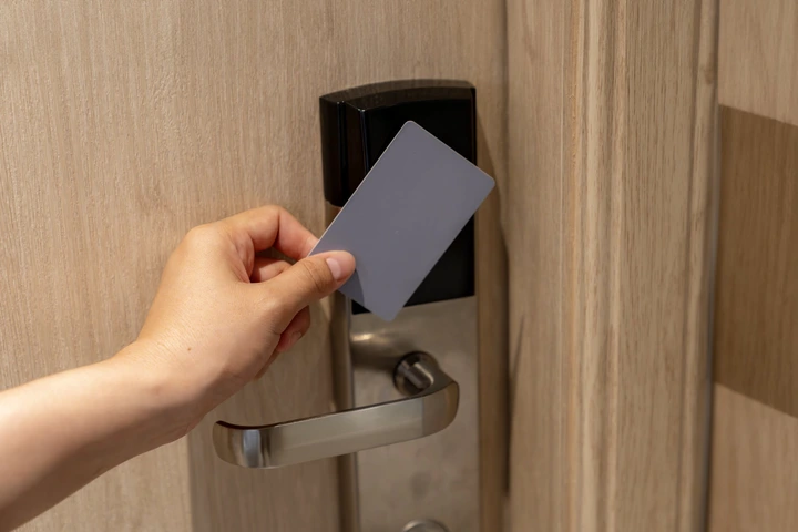 A hand holding a key card approaching a door lock, possibly in a hotel or office setting