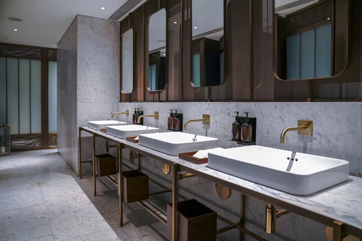Modern public restroom with sleek marble countertops, several rectangular sinks, gold-tone faucets, and large mirrors