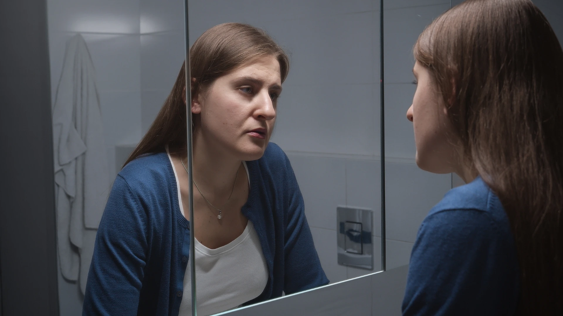 Woman looking sadly in the mirror.