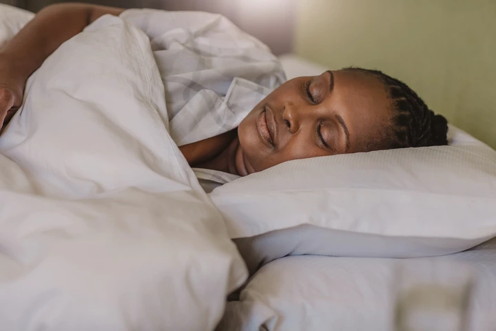 Person sleeping peacefully in bed, head resting on a pillow, covered with a white blanket