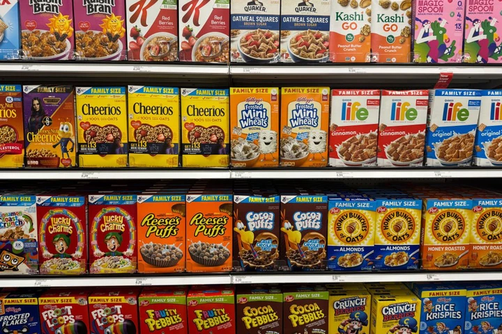 Grocery store shelf displaying a variety of boxed cereals, including Cheerios, Reese&#x27;s Puffs, and Lucky Charms