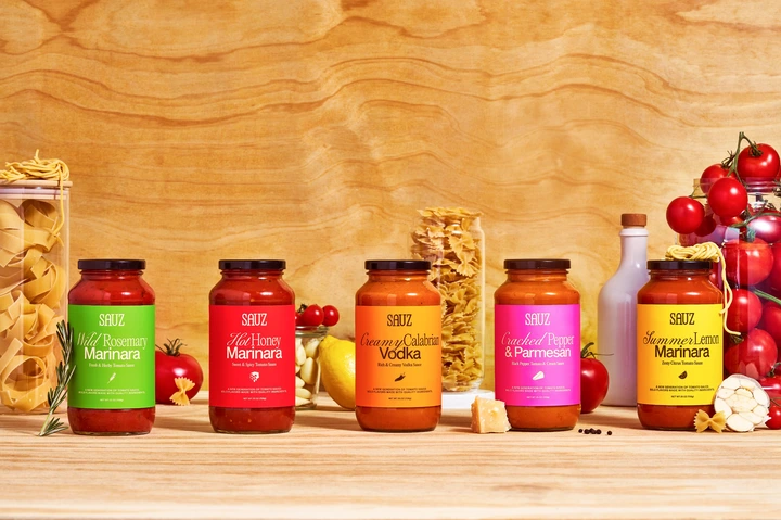 Five jars of SABUZ pasta sauce in various flavors are arranged on a kitchen counter surrounded by pasta and vegetables