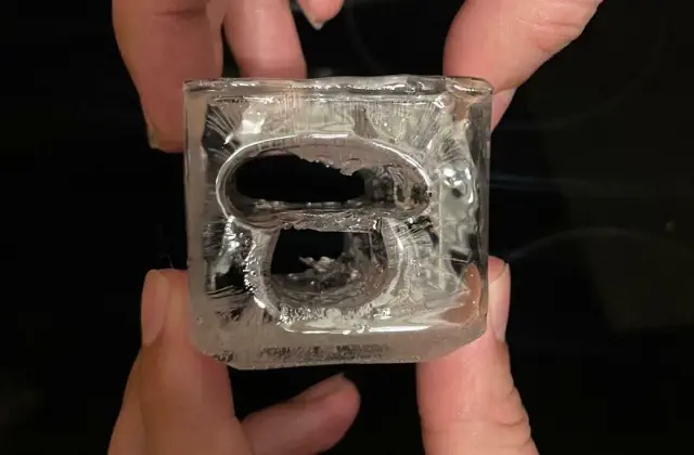 Ice cube shaped like a bottle opener held between fingers.