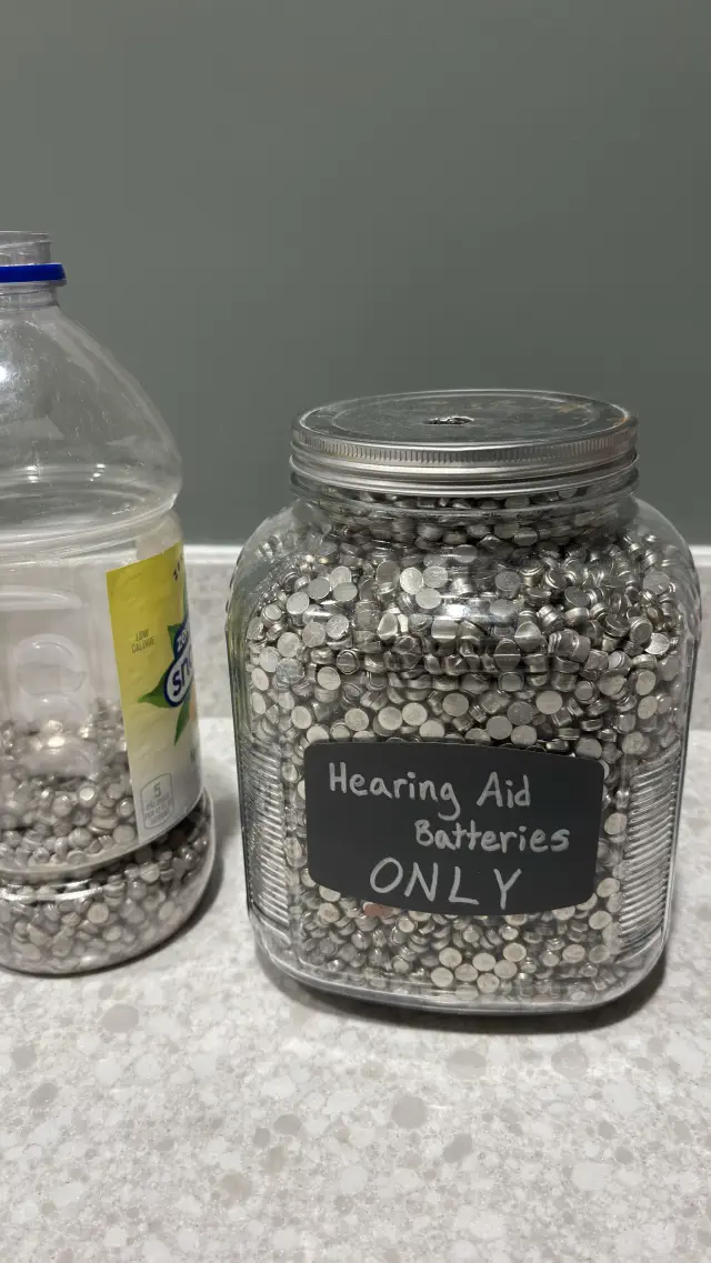 Jars filled with small batteries; one labeled &quot;Hearing Aid Batteries ONLY.&quot;