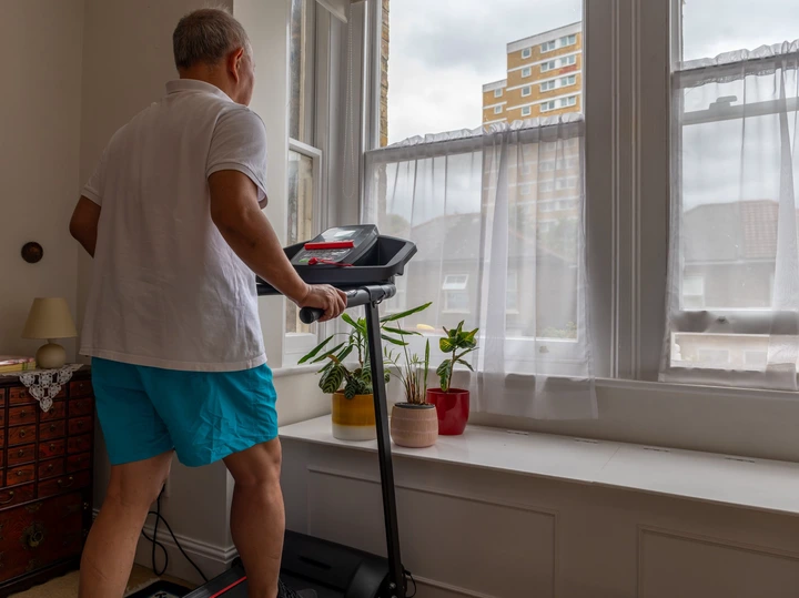 A person walks on a treadmill at home, facing a window with plants, creating a peaceful and healthy indoor exercise setting