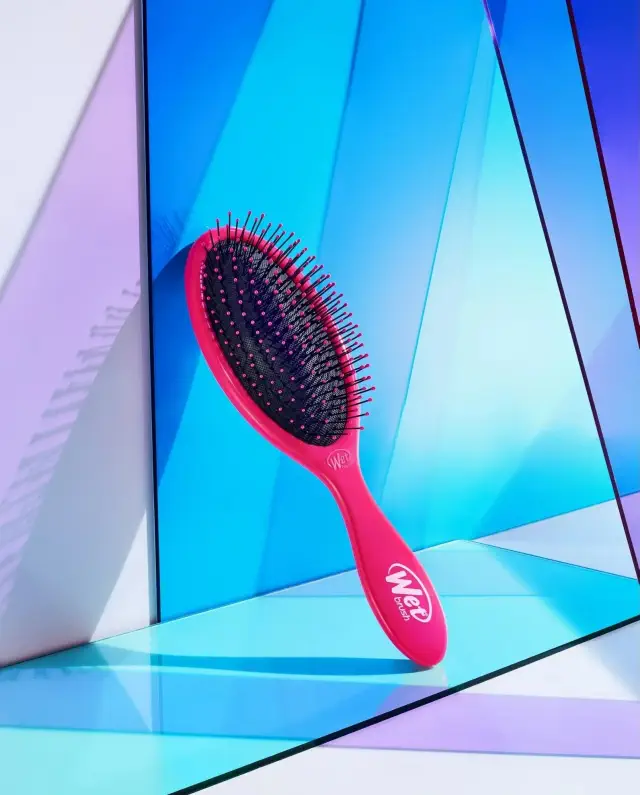 Hairbrush with black bristles on a pink base, angled against geometric panels, featured for shopping in an article