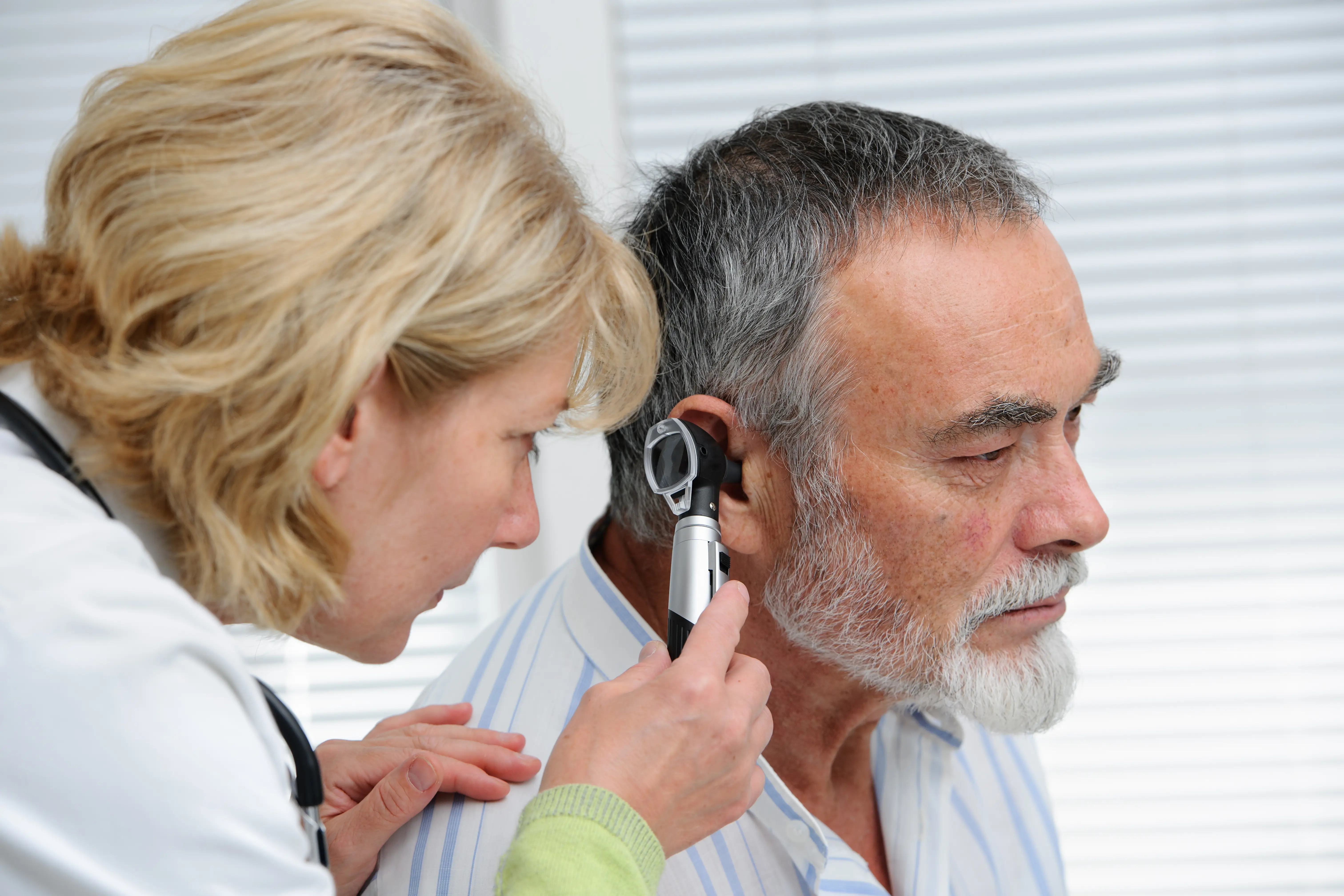 A doctor peers into a man's ear using an otoscope.