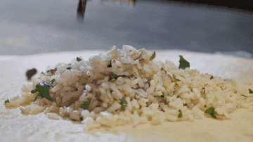 A close-up of rice being spread on a tortilla with chopped herbs, suggesting a fresh and appetizing meal preparation