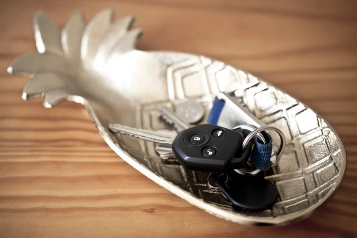 A decorative pineapple-shaped dish holds car keys and other keys on a wooden surface
