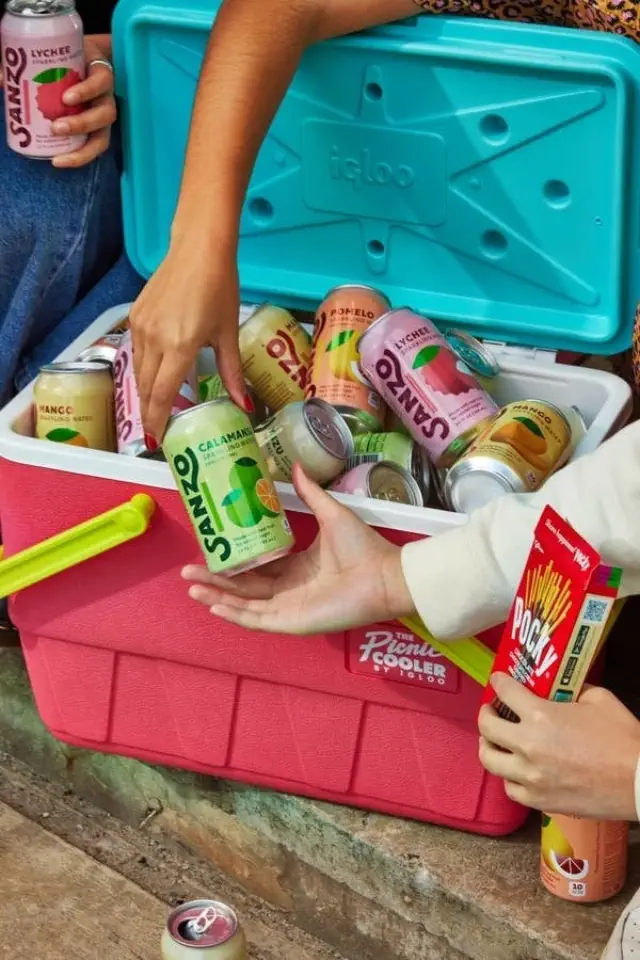 People reaching into a cooler for Sanzo sparkling water cans. One person also holds a pack of Pocky sticks
