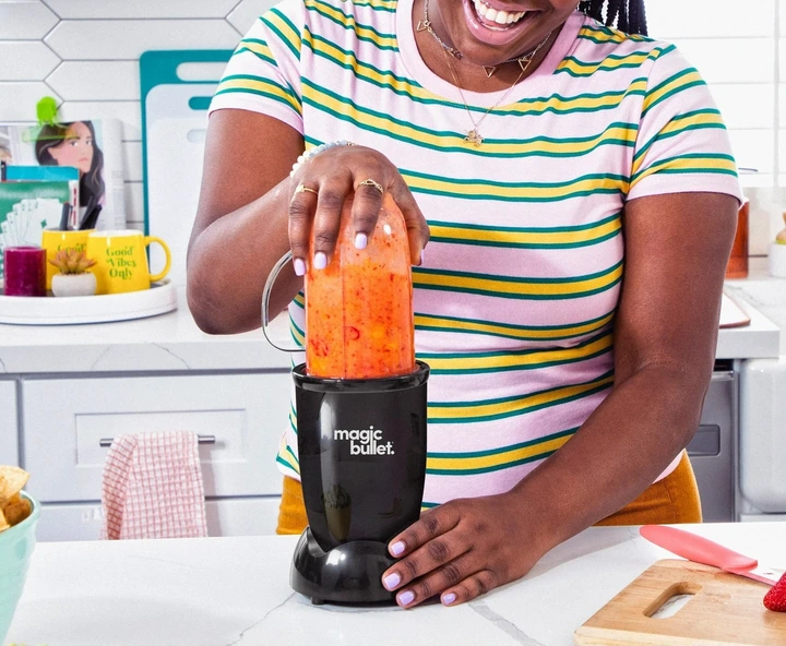 Person using a Magic Bullet blender in a kitchen, making a smoothie