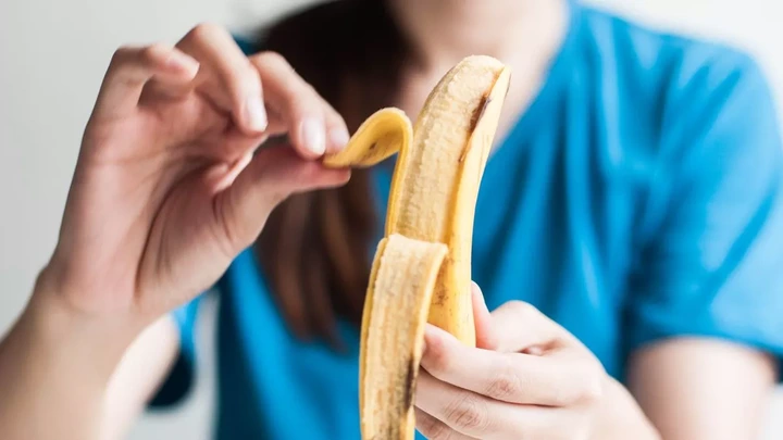 Close-up view of a young Southeast Asian woman in blue casual clothing is holding a fresh yellow ripe banana