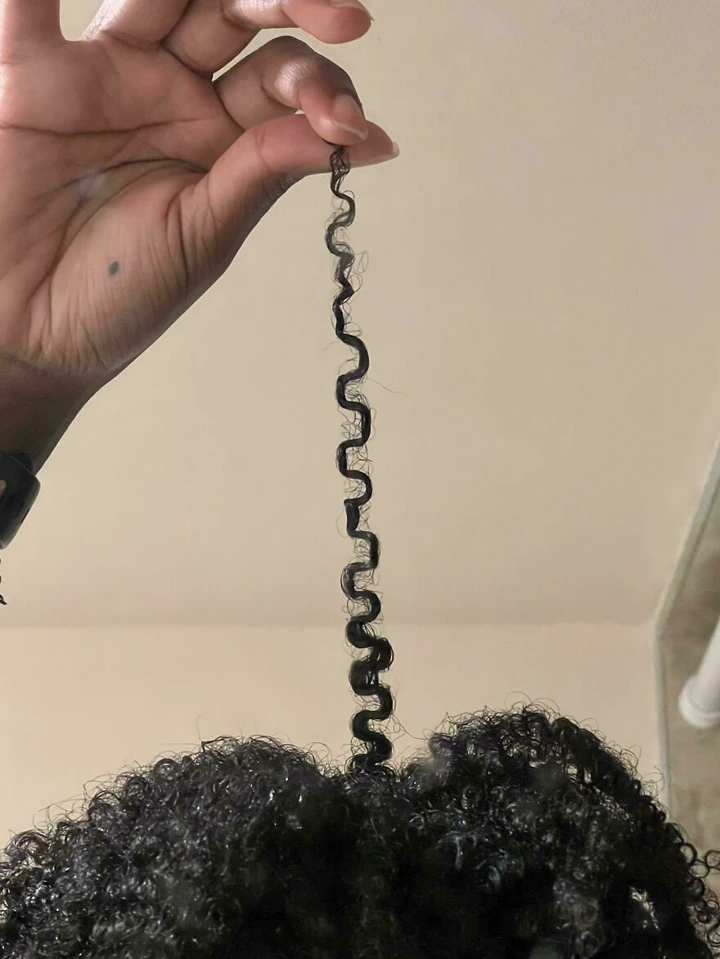 Curly hair strand resembles a spiral shape, held by a hand.