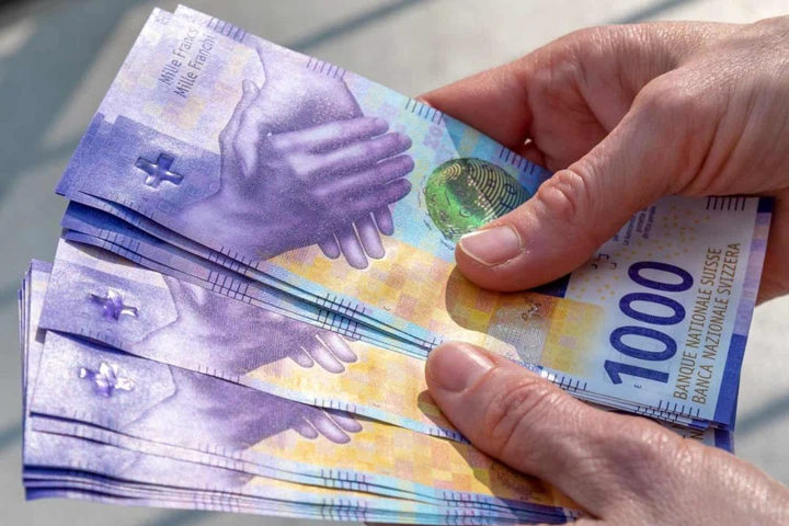 two hands gripping a bundle of Swiss franc currency