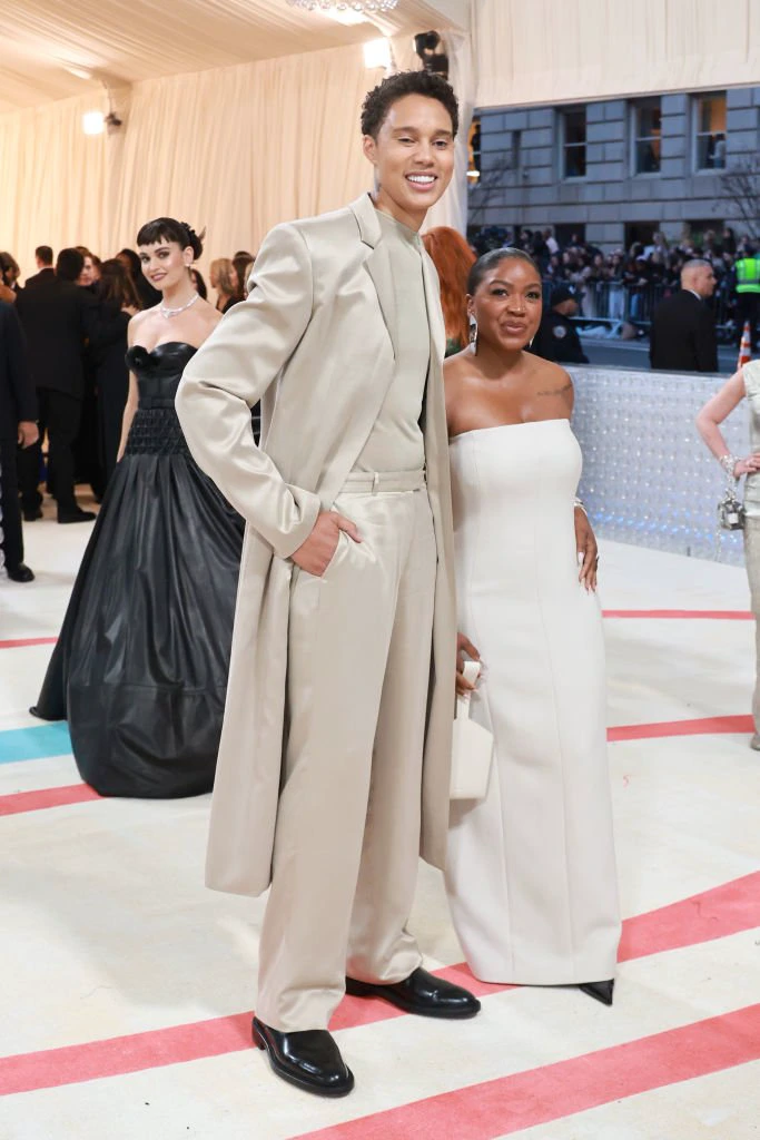 Brittney and Cherelle on a red carpet. Brittney wears a long coat and suit, Cherelle a strapless dress. Background shows an elegant event setting. Cherelle comes up to Brittney&#x27;s chest