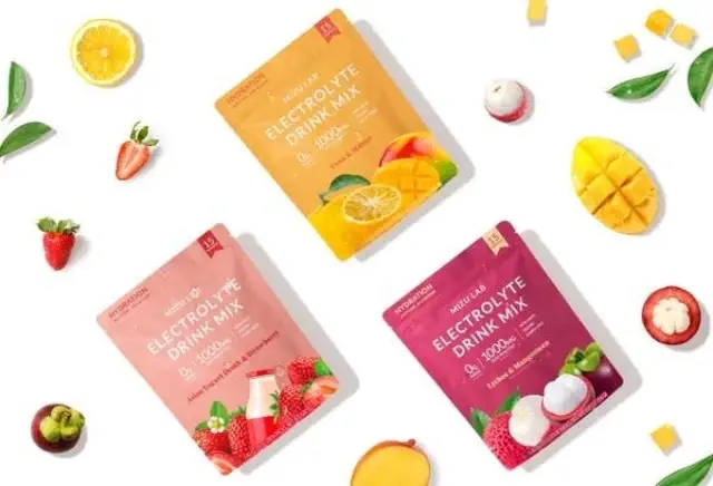 Three packets of electrolyte drink mix in assorted flavors are displayed with fruits like strawberry and mango surrounding them
