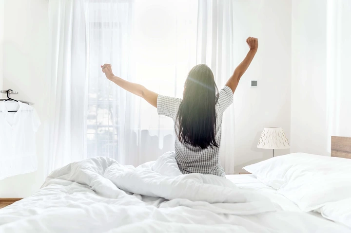A woman waking up in a bed with white bedding.