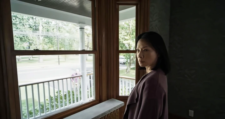 Person standing indoors, gazing out of a window onto a porch with a thoughtful expression