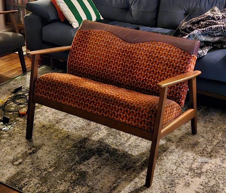 Matthew McCallum A bright orange and red subway seat converted into a couch with wooden armrests and legs in a living room.