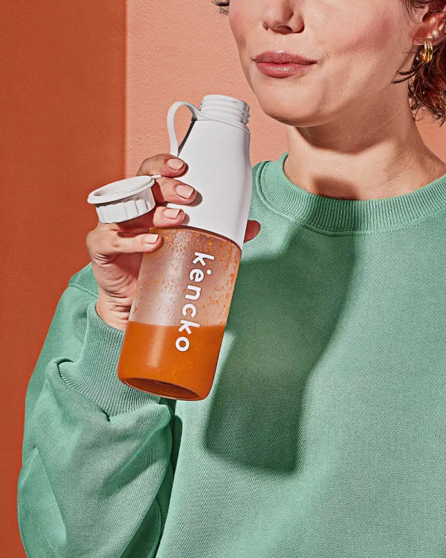 Person holding a Kencko smoothie bottle, wearing a casual green sweatshirt