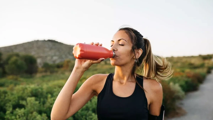 Fit young Woman in black sportswear drinking water from a reusable metal bottle after running workout
