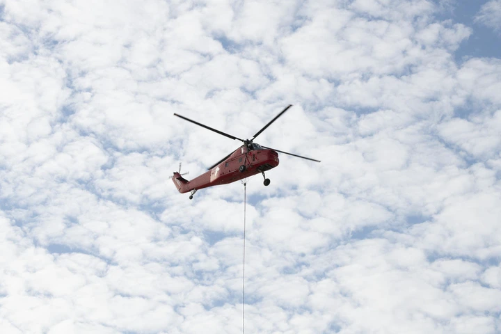 A helicopter is positioned to carry a rooftop pedestal.