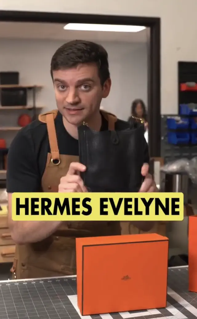 Person in workshop holding a black leather Hermes Evelyne bag, with orange Hermès box on table