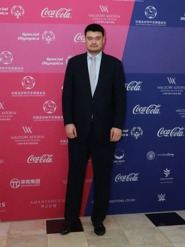 Yao in a suit on a red carpet at a Special Olympics event with sponsor logos in the background
